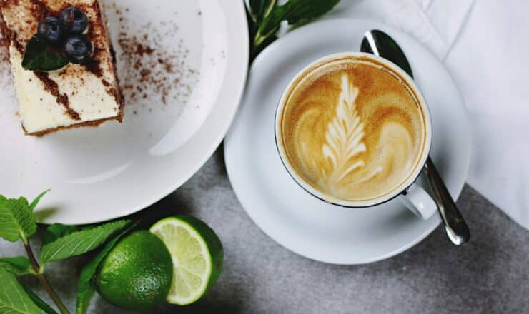 flat lay photography of coffee in teacup near plate of sliced cake